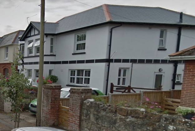 A screenshot from Google Street View. It shows a large, white house with a dark line detail under the upper windows.